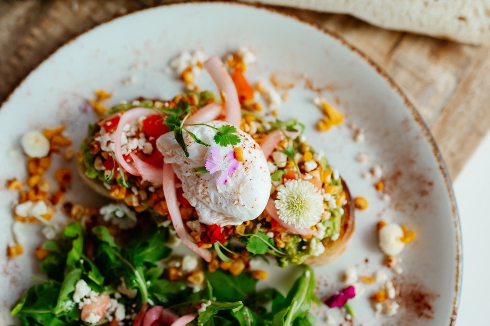 Avocado toast topped with roasted corn, pickled onion, cotija and a poached egg